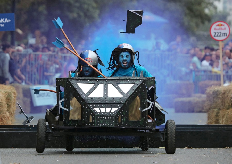 Two men in costume ride a small homemade vehicle through an obstacle course.