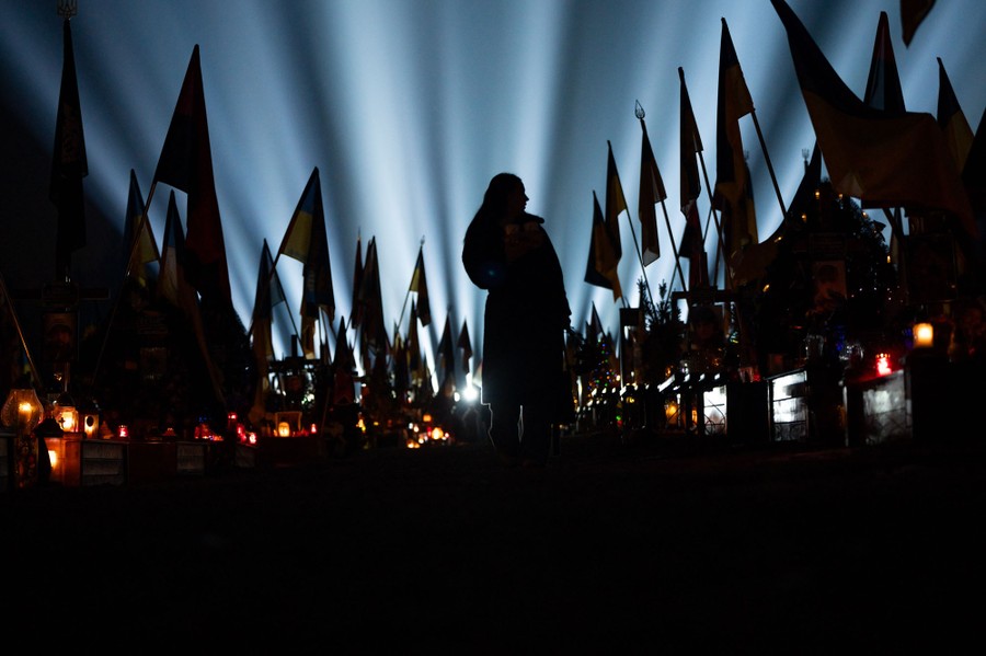 A person stands in silhouette, beneath rays of light over a cemetery decorated with flags.
