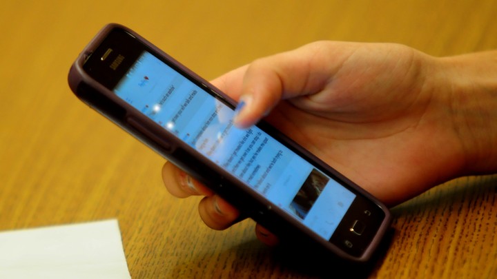 A student's hand is shown holding an iPhone.