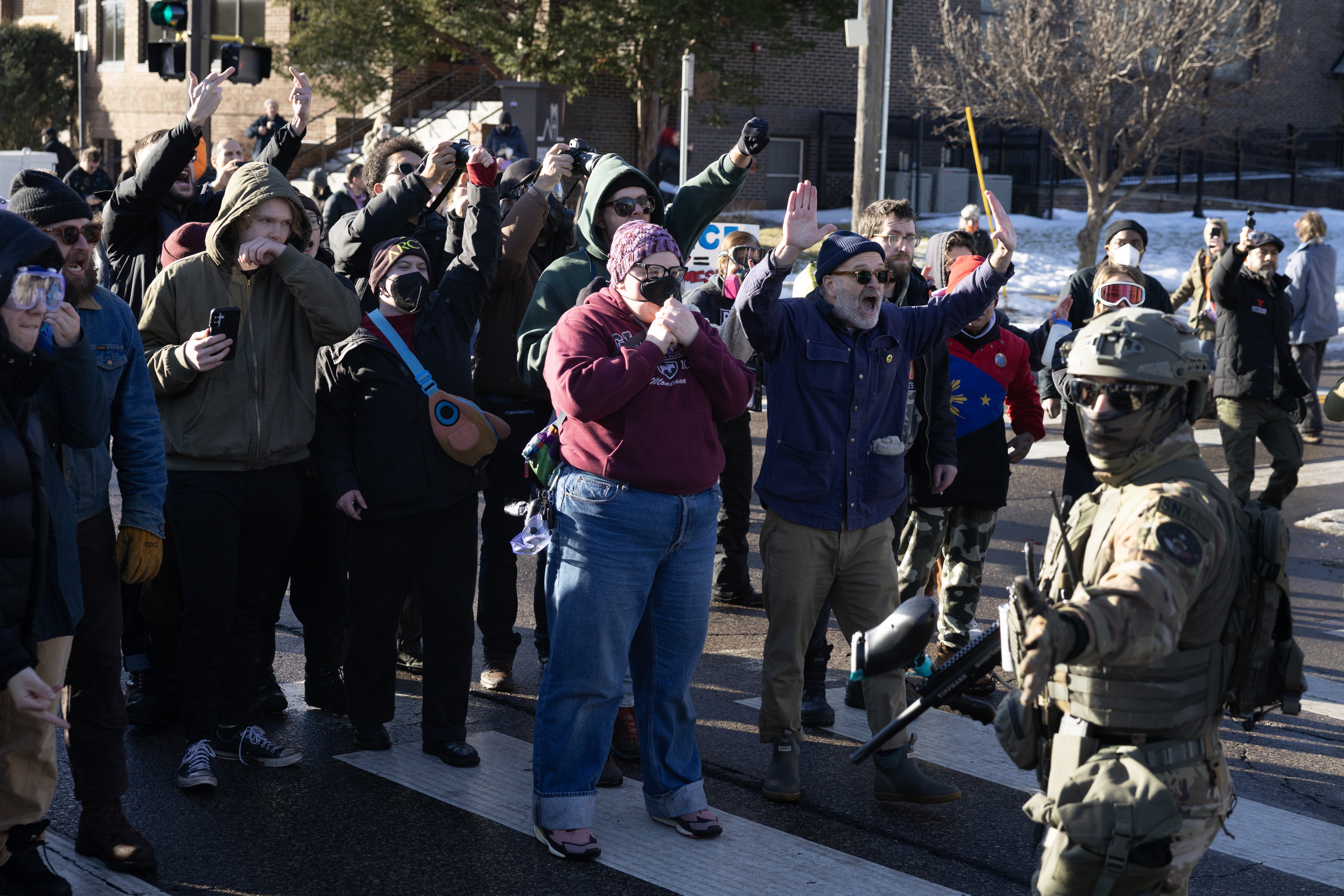 A group of people stand together in a street, confronting masked federal officers during an immigration raid.
