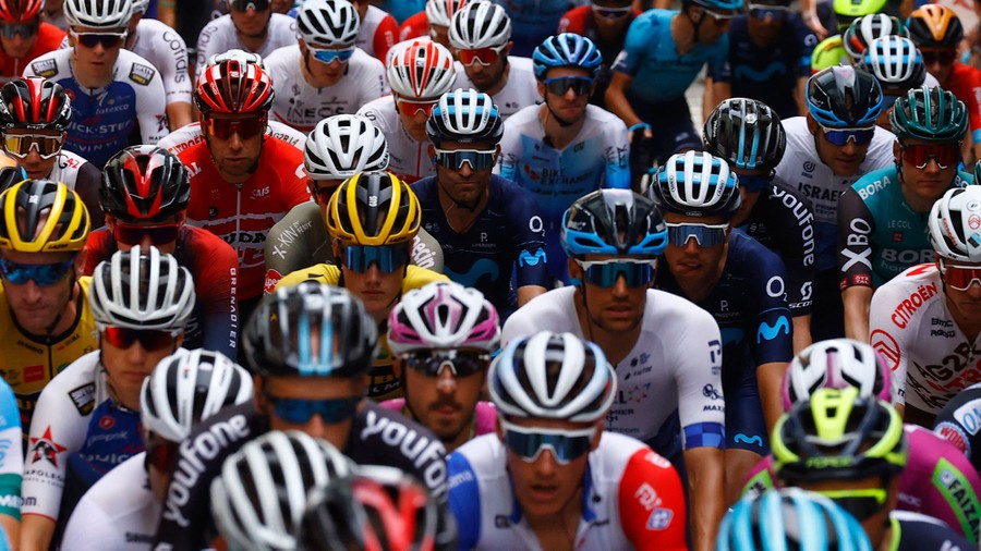 Dozens of professional cyclists wait, helmeted, ready to start a race.