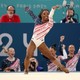 Teammates cheer in the background as a gymnast completes a floor-exercise routine.
