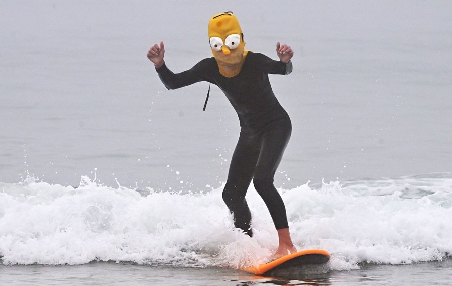 A surfer in a Homer Simpson mask catches a wave.