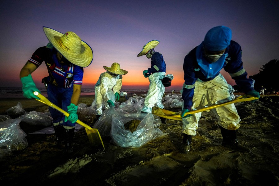Several workers clean spilled oil off a beach.