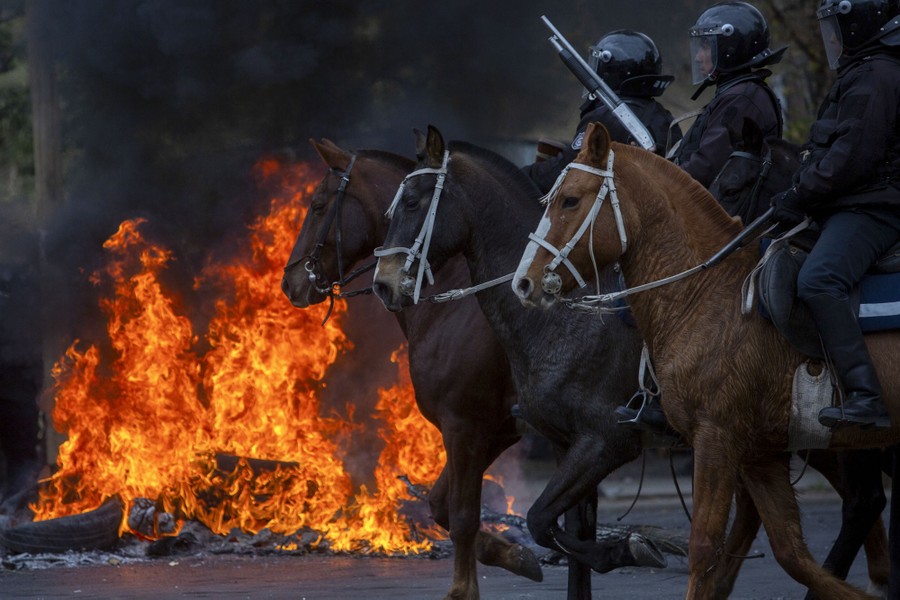 Riot police on horseback ride past a fire burning in a street.