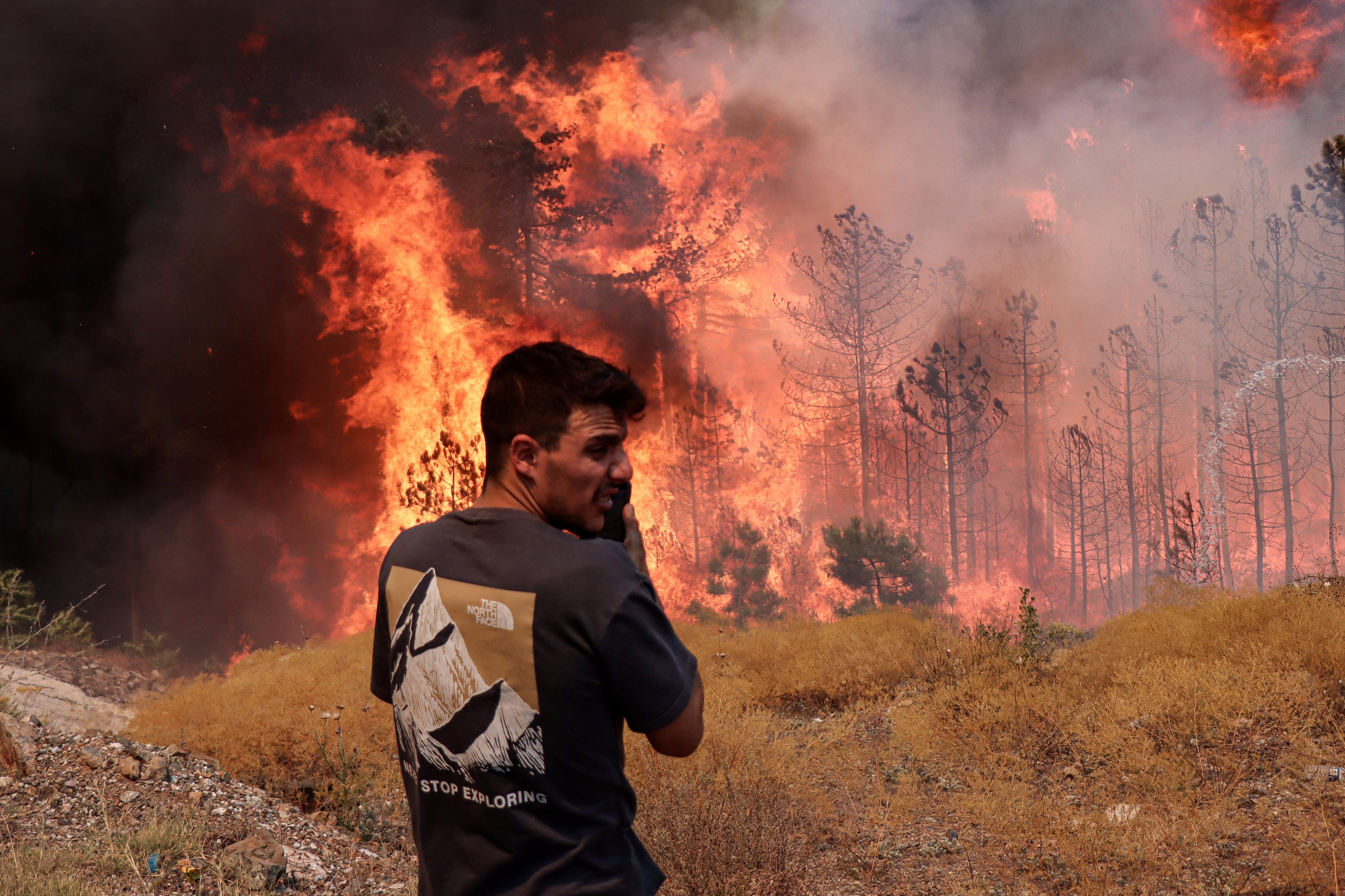 A person looks at a nearby wildfire that is burning through a forest.