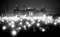 A black-and-white photo of protesters holding up lights outside the Reichstag building