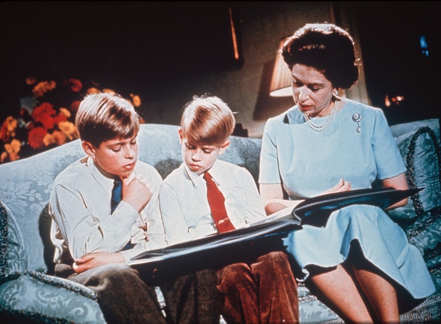 The Queen sits on a couch with her two young sons, looking at a photograph album.