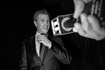 Black-and-white photo of Gavin Newsom in front of a mic held out by a hand