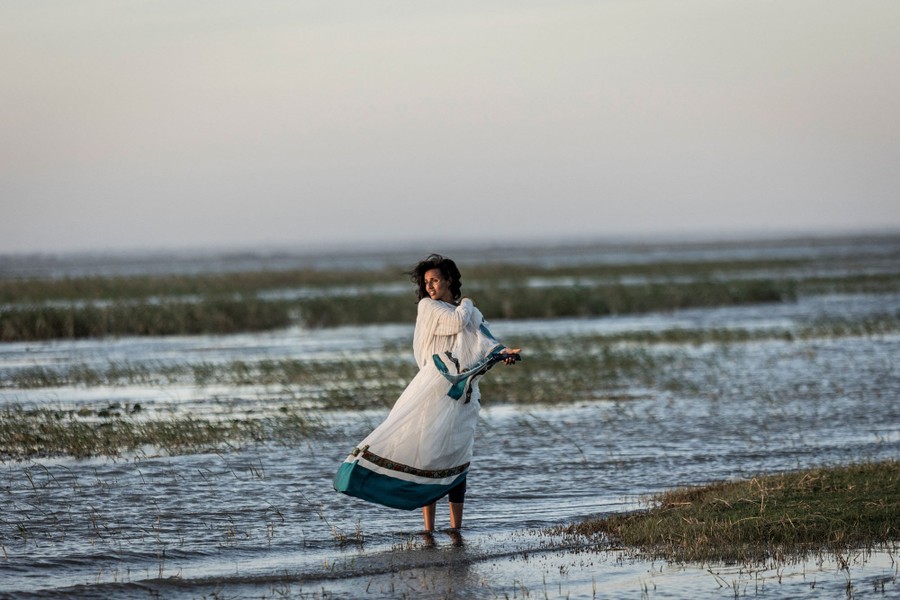 A woman stands at the edge of a lake, looking into the distance.
