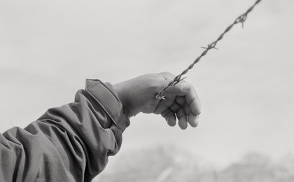 Raul Rodriguez's hand rested on barbed wire in black and white.