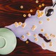 A green bowl upside down on a reddish-brown wood table, with spilled milk and Cheerios to its right. A silver spoon lies upside down in the milk.