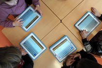 Children sit a table using tablet computers