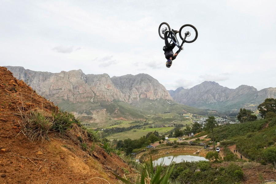 A mountain bike rider upside down in mid-air above a steep mountain track