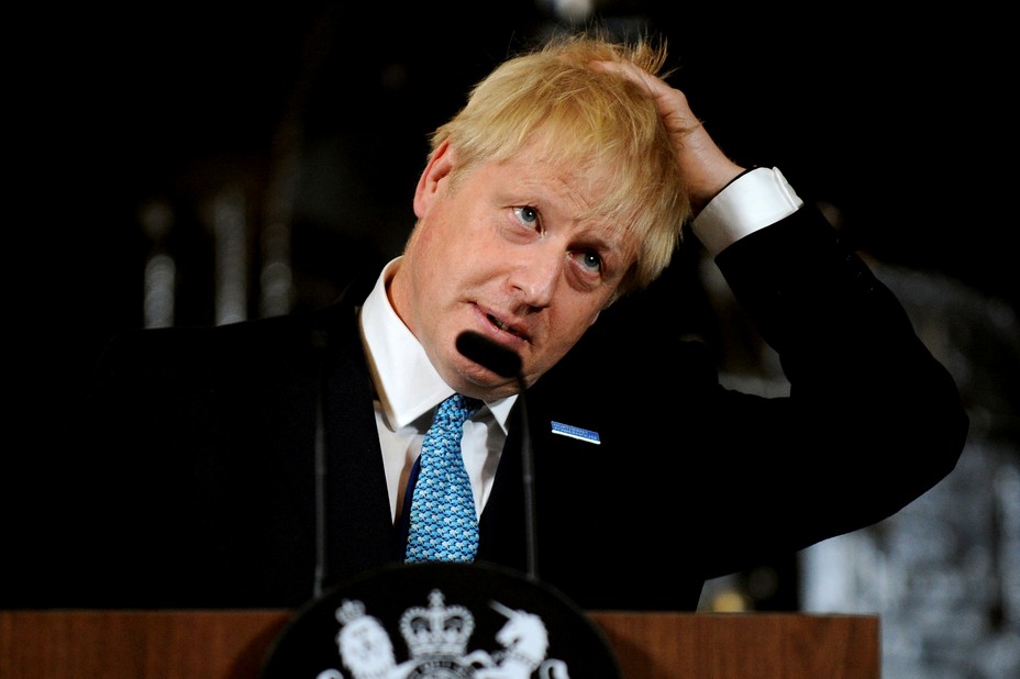 Boris Johnson stands in front of a lectern and runs his hand through his hair.