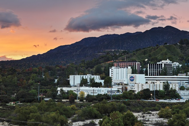 photo of large JPL complex of buildings, one with NASA logo, at sunset, with mountain in backgroun