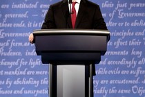 A politician's body at a lectern with words out of focus behind him.