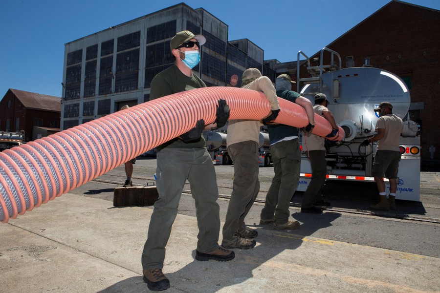 Several people maneuver a large plastic tube to the back of a tanker truck carrying water and fish.
