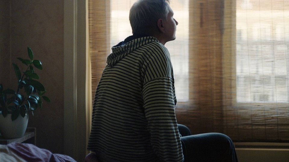 A person sits on top of a bed and gazes toward a window.