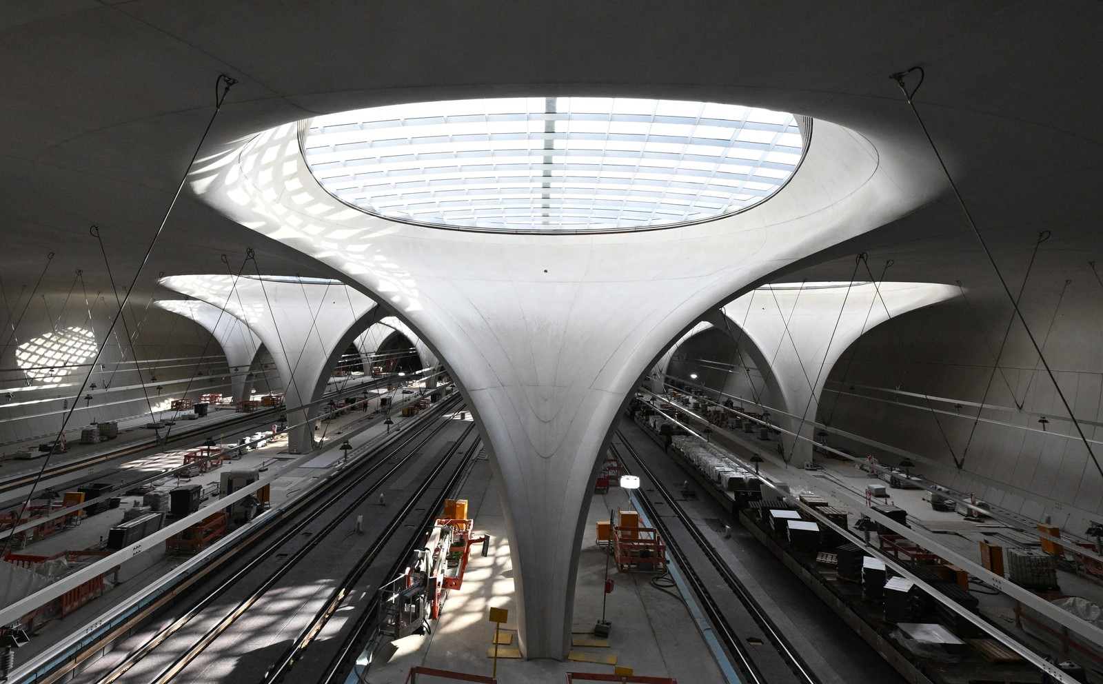 The interior of a modern train station under construction, featuring swooping pillars opening up to large circular skylights