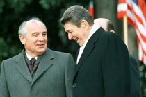 President Ronald Reagan stands with former Soviet leader Mikhail Gorbachev and laugh in front of an American flag.