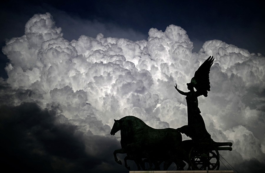 Dramatic clouds pass above a statue.