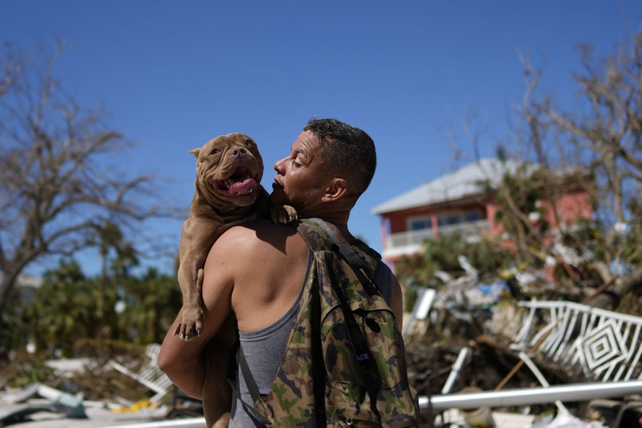 A person carries a dog through a storm-damaged neighborhood.
