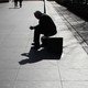 The silhouette of a man looking at his phone as he sits on a long bench