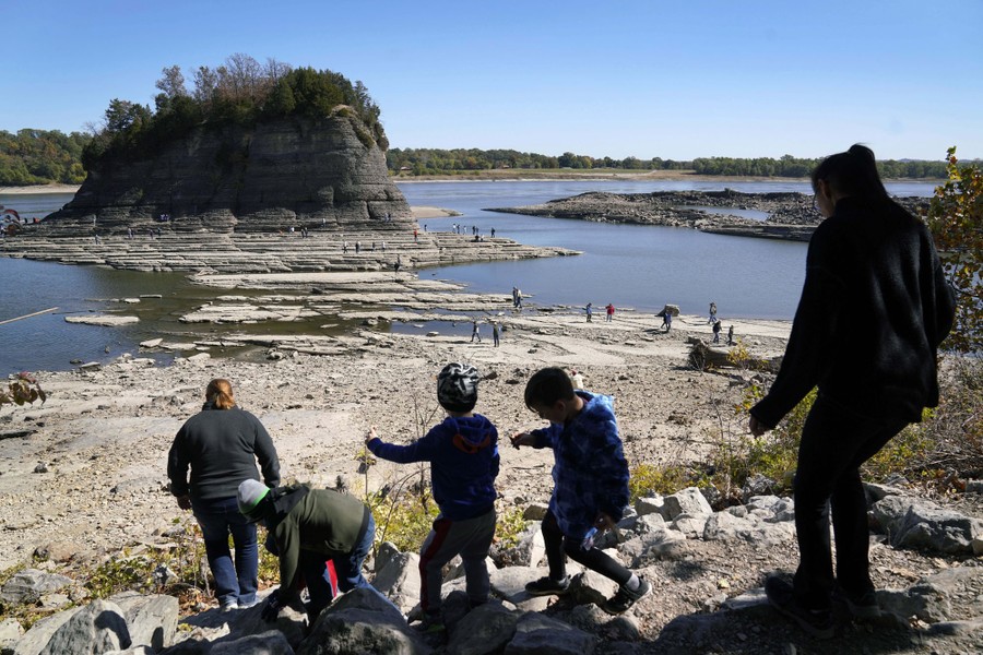 People climb down a rocky hill, heading toward a rock outcrop in a river with very low water.