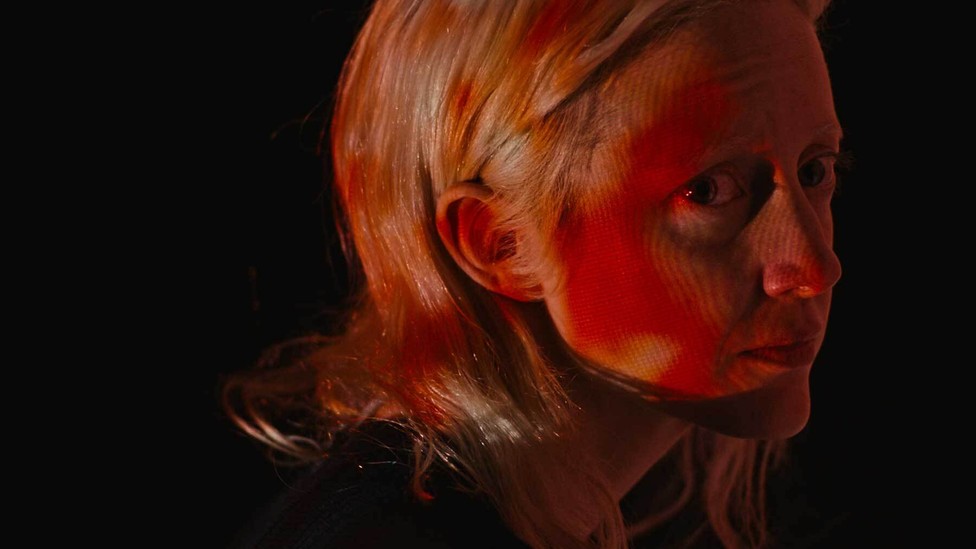 A close-up of a woman with splotchy red light on her face