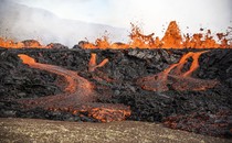 Lava erupts and flows across a valley floor.