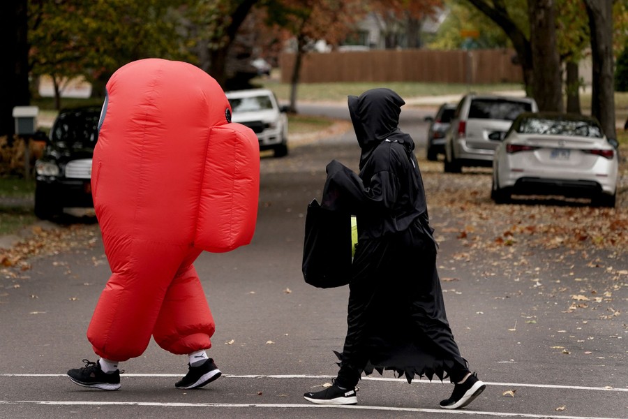 Two people in costume walk across a crosswalk in a residential neighborhood.