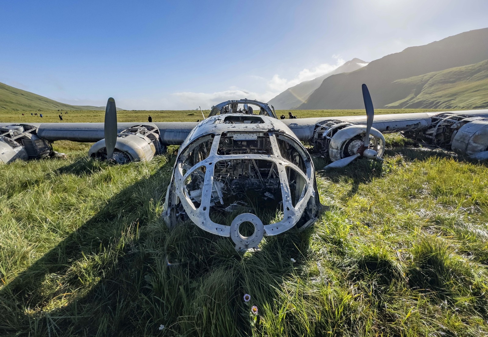 The shell of a crashed WWII-era bomber aircraft sits on grassy ground.