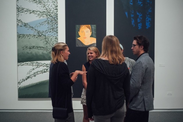 A group of students chats in front of artistic canvases.
