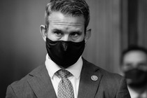 Representative Adam Kinzinger wears a black mask and suit