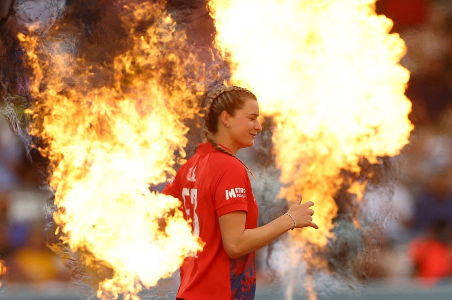 A cricket player runs between two jets of flame.