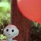 An AI robot with a slight smile stands next to red and yellow balloons.