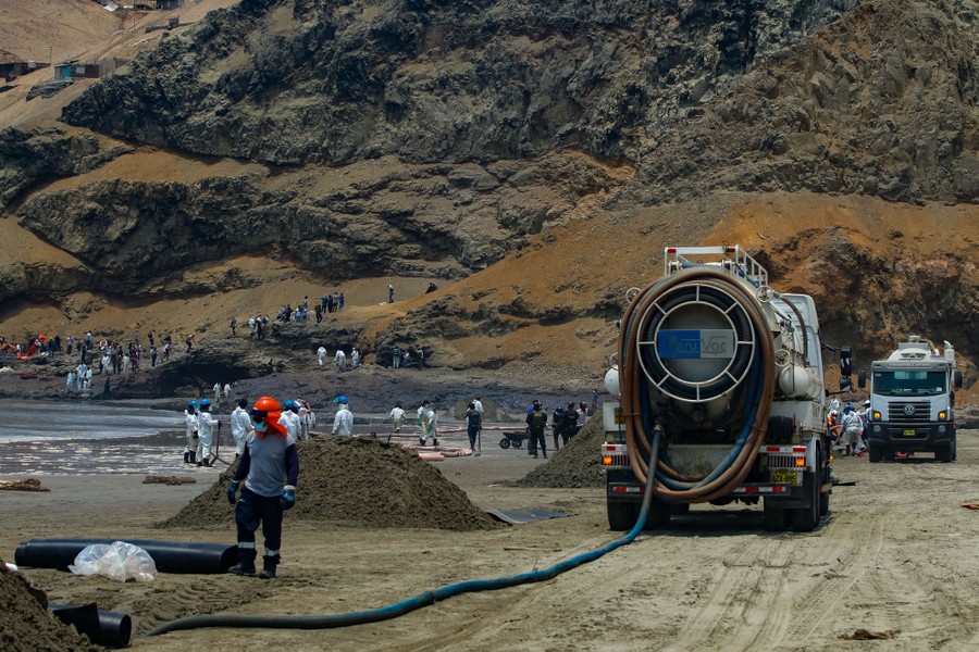 Dozens of people work to clean oil from a beach.