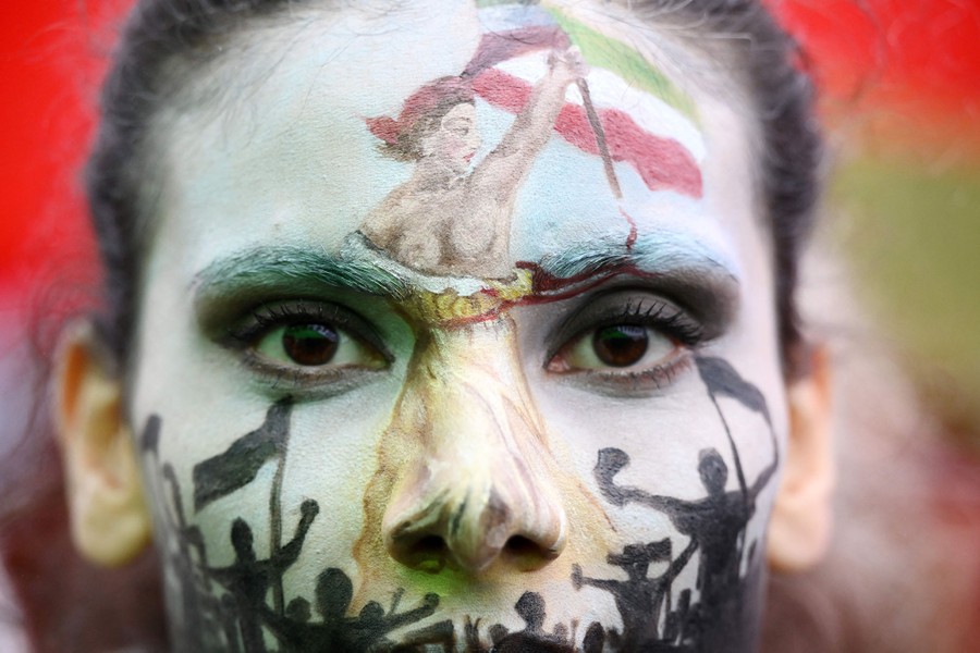 A protester wears elaborate face paint depicting a woman carrying a flag and leading a crowd