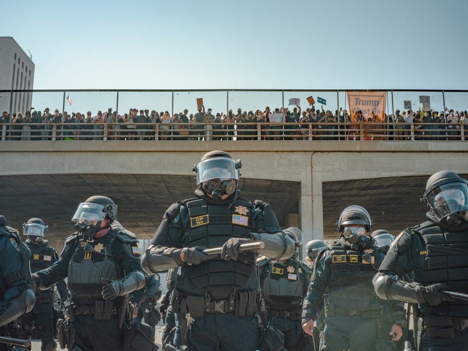 Police stand in a line in front of a bridge with people standing on it.