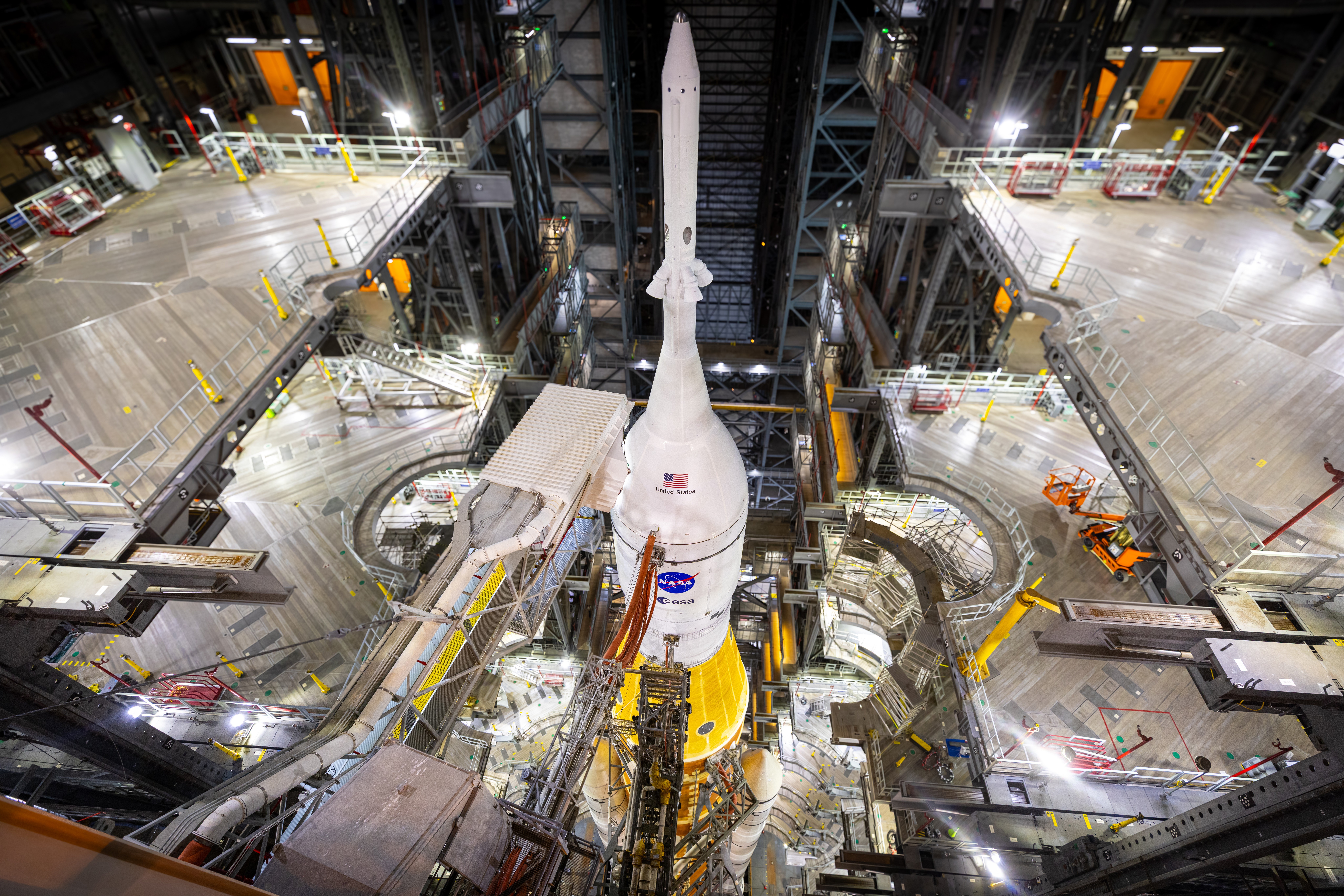 A view looking down on a rocket from a high platform inside a very tall building, with multiple retractable decks on either side of the rocket.