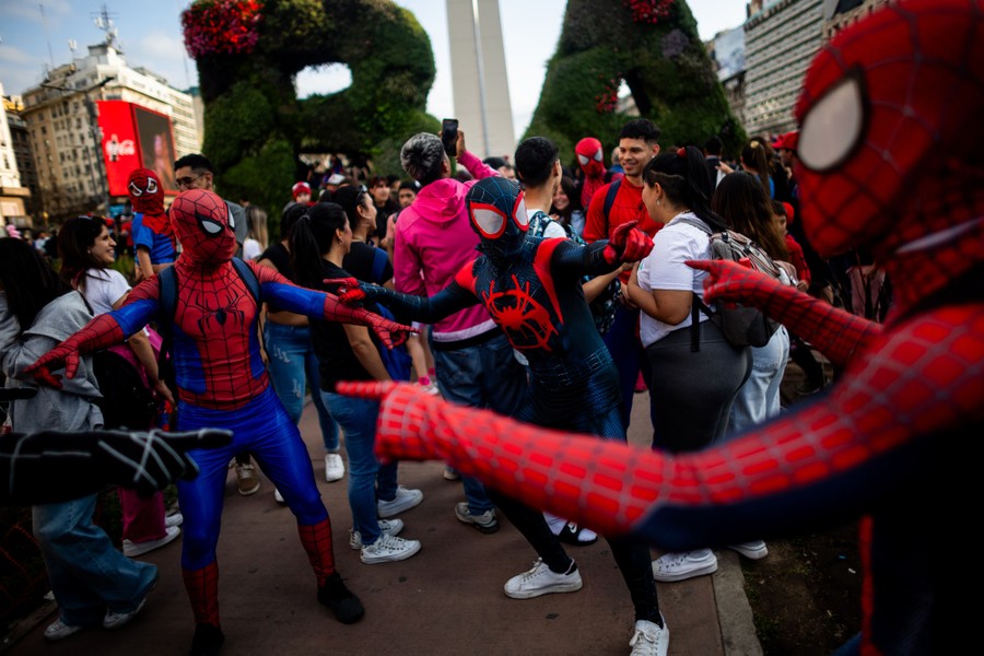 Several people in a crowd, dressed as various versions of Spider-Man, point at one another.