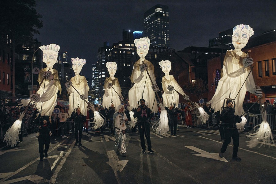 A half-dozen tall puppets are operated during a Halloween parade.