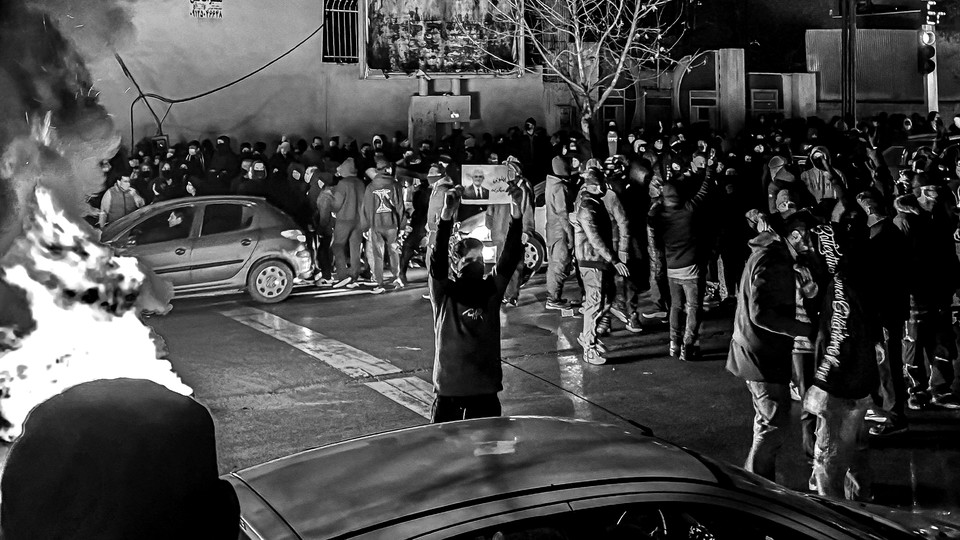 Black-and-white photograph of protesters in Iran gathering in the streets with a fire in the foreground