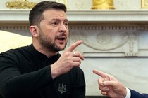 A man with a trim beard in a black collarless shirt pointing, with another man's finger pointing back.