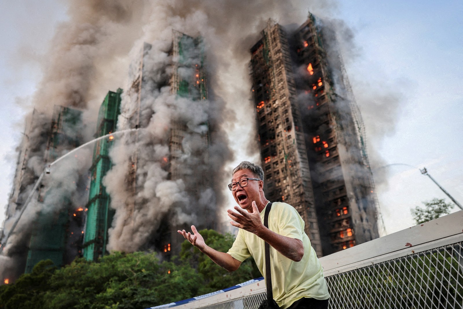A man reacts emotionally while standing outside a burning complex of tall residential buildings.