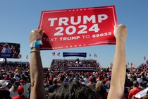 Photo of a "Trump 2024" sign being raised at a Trump rally