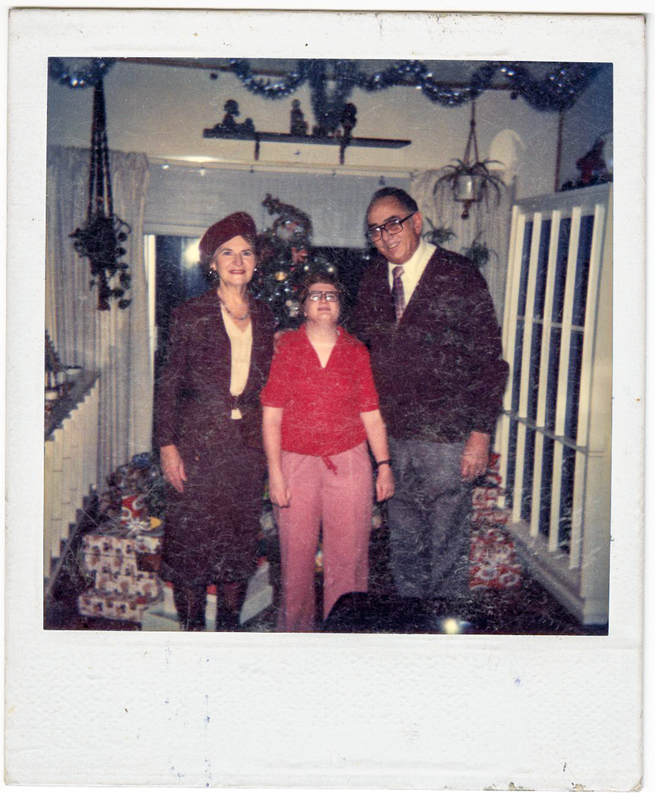polaroid photo of dressed-up woman and man on either side of shorter woman wearing red