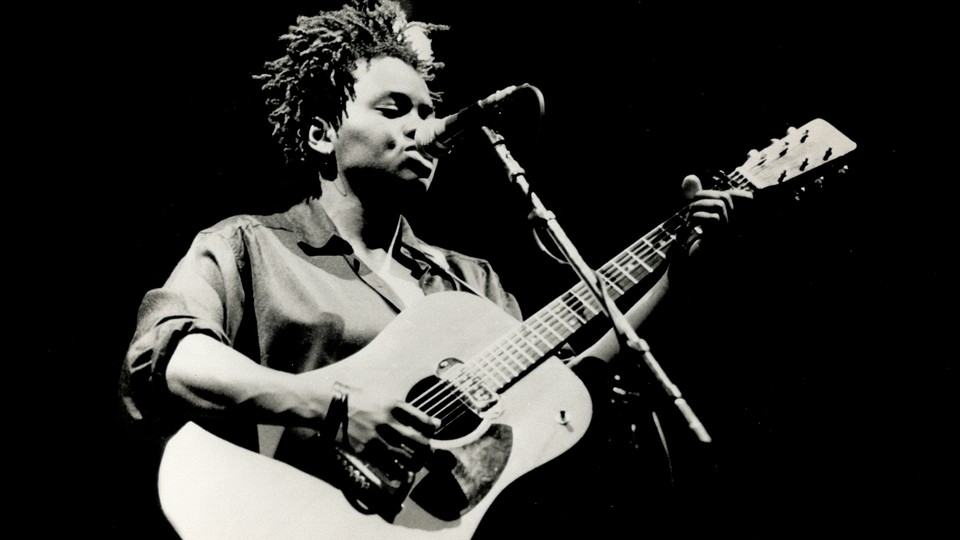 A black-and-white photo of Tracy Chapman playing the guitar and singing.