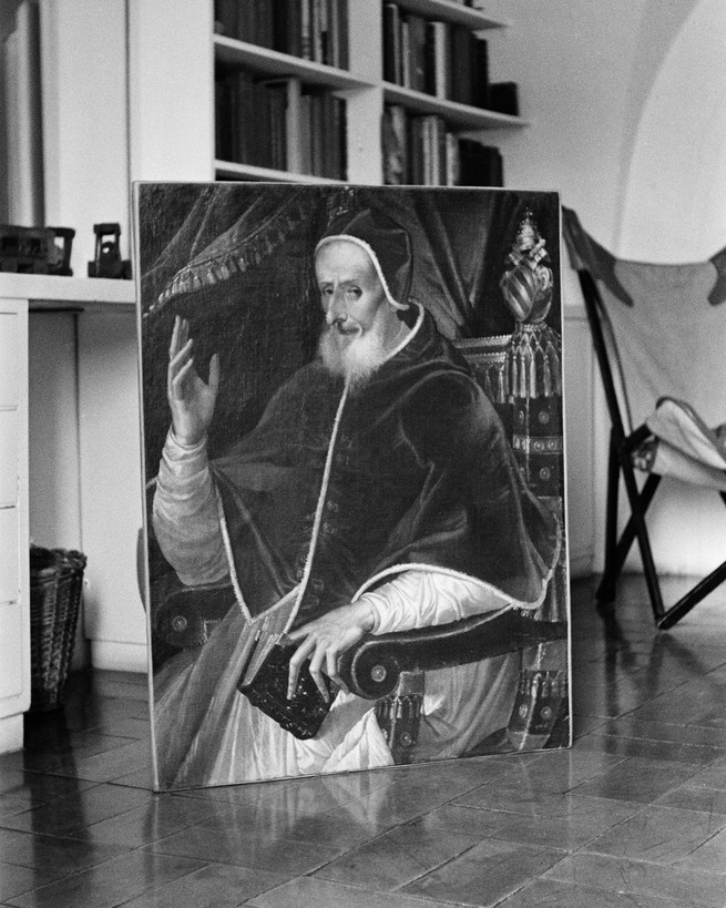 A portrait of a priest leans against a bookshelf